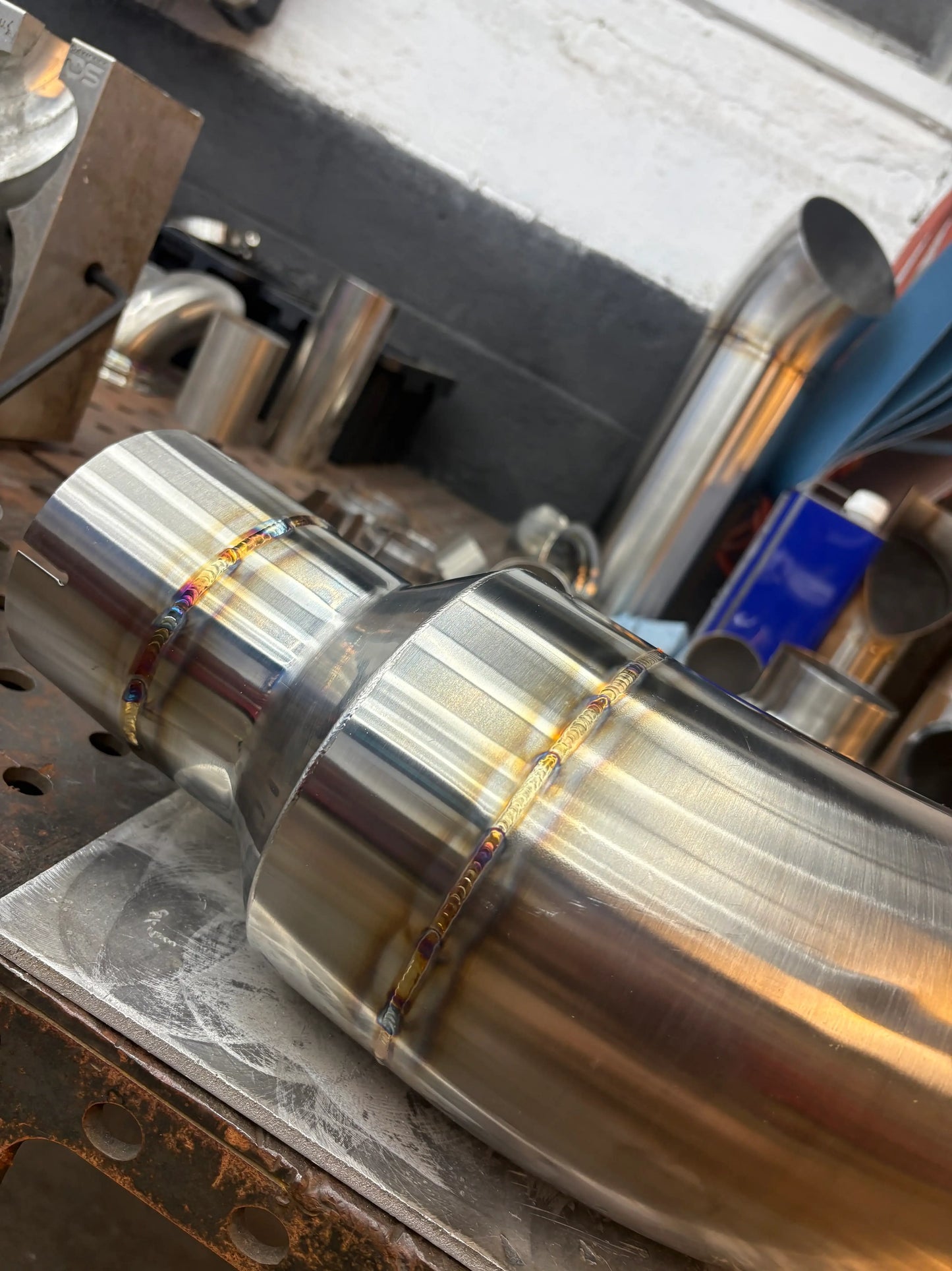 Stainless steel exhaust pipe with rainbow weld seams on workshop table