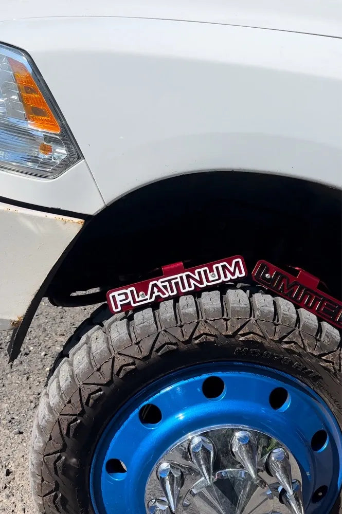 Close-up of truck front left wheel with blue rim, rugged tire, and platinum badge under fender
