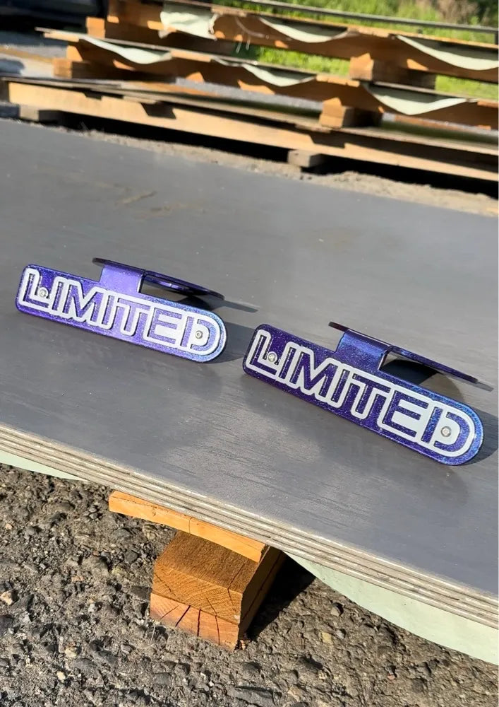 Pair of metallic blue LIMITED car badges displayed outdoors on a metal surface