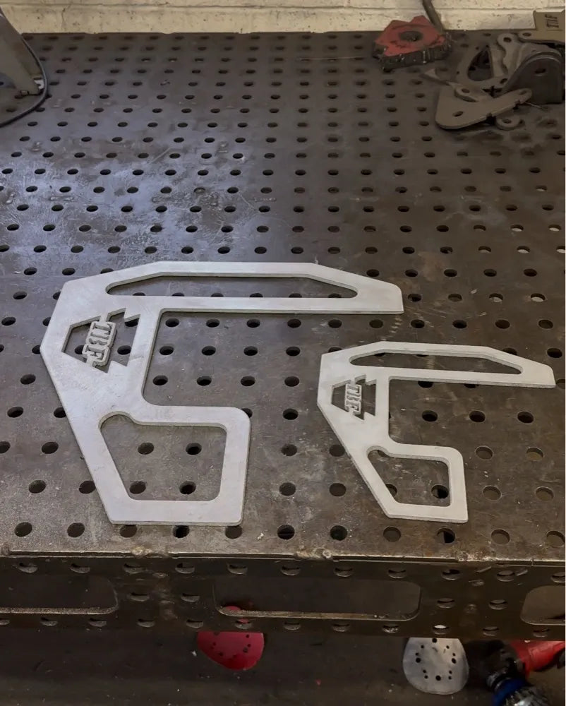 Two metal fabrication brackets with geometric cutouts on a perforated workbench