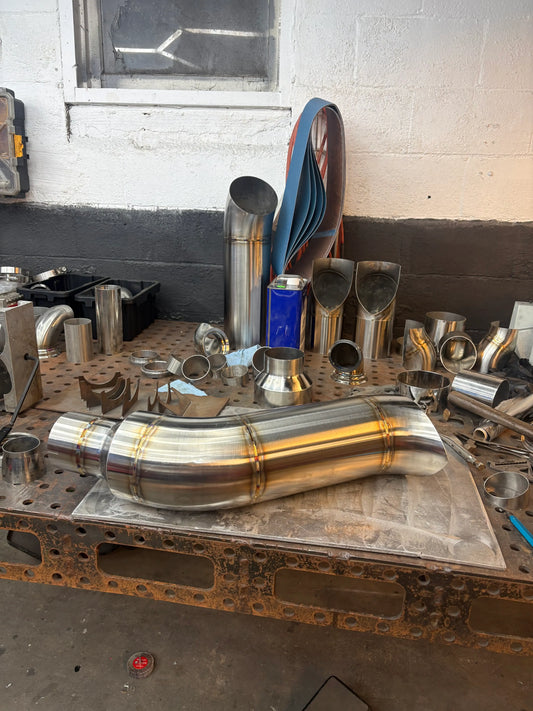 Custom stainless steel exhaust pipes and fittings on workshop table, precision welded for performance vehicles
