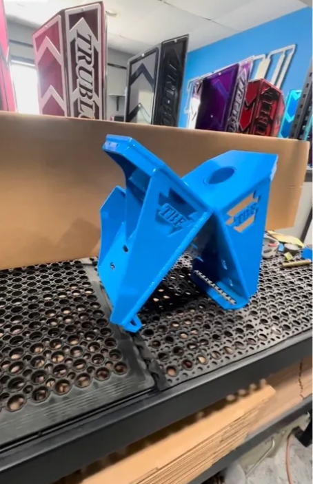 Blue metal fabrication jack stand with cutout logo in workshop setting