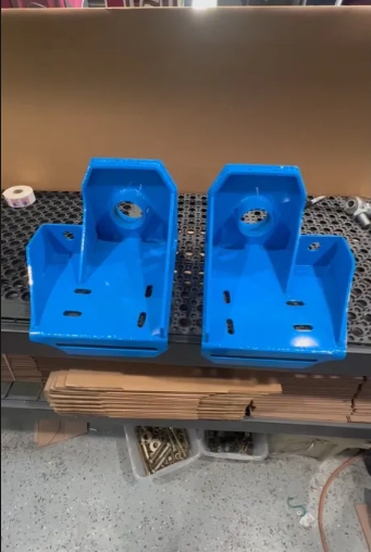 Pair of blue metal brackets with mounting holes on a workshop table