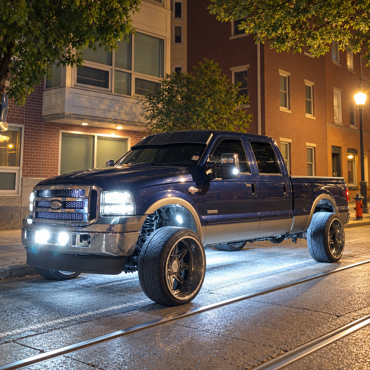 Lifted dark blue Ford Super Duty with a TRUBLU Fab V drop visor and underglow on a city street at night