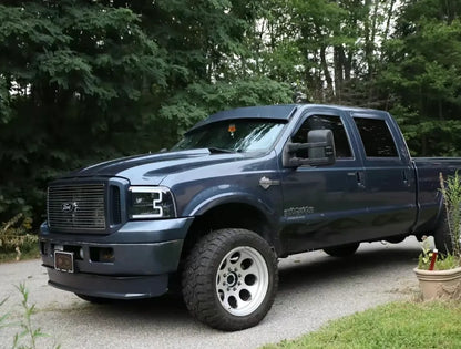 Blue Ford Super Duty pickup truck parked outdoors on a driveway surrounded by trees