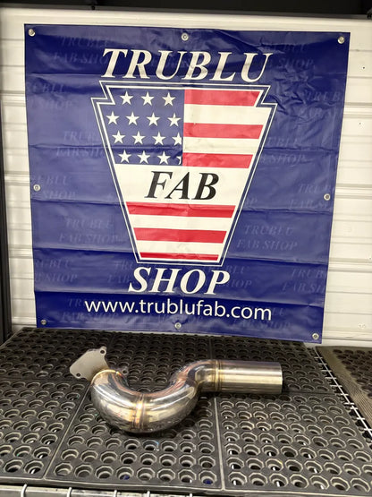 Stainless steel exhaust pipe with welded bends on a metal workbench in a fabrication shop.