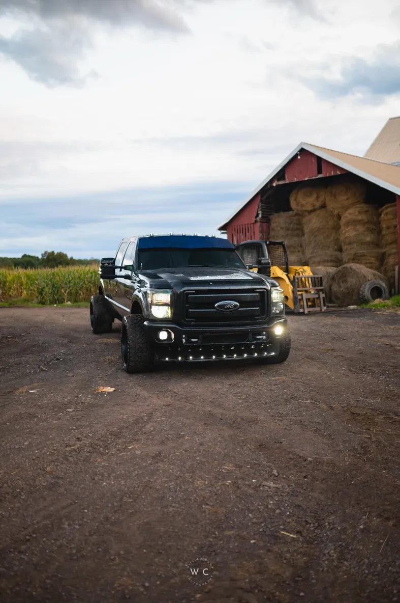 Black lifted Ford pickup truck with LED lights parked on a farm by a barn and hay bales