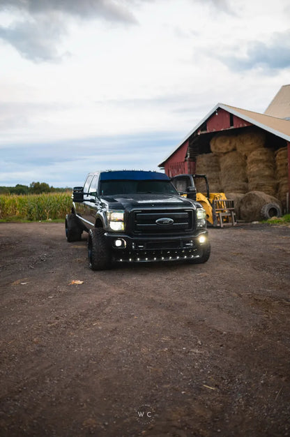 Black lifted Ford pickup truck with LED lights parked on a farm by a barn and hay bales