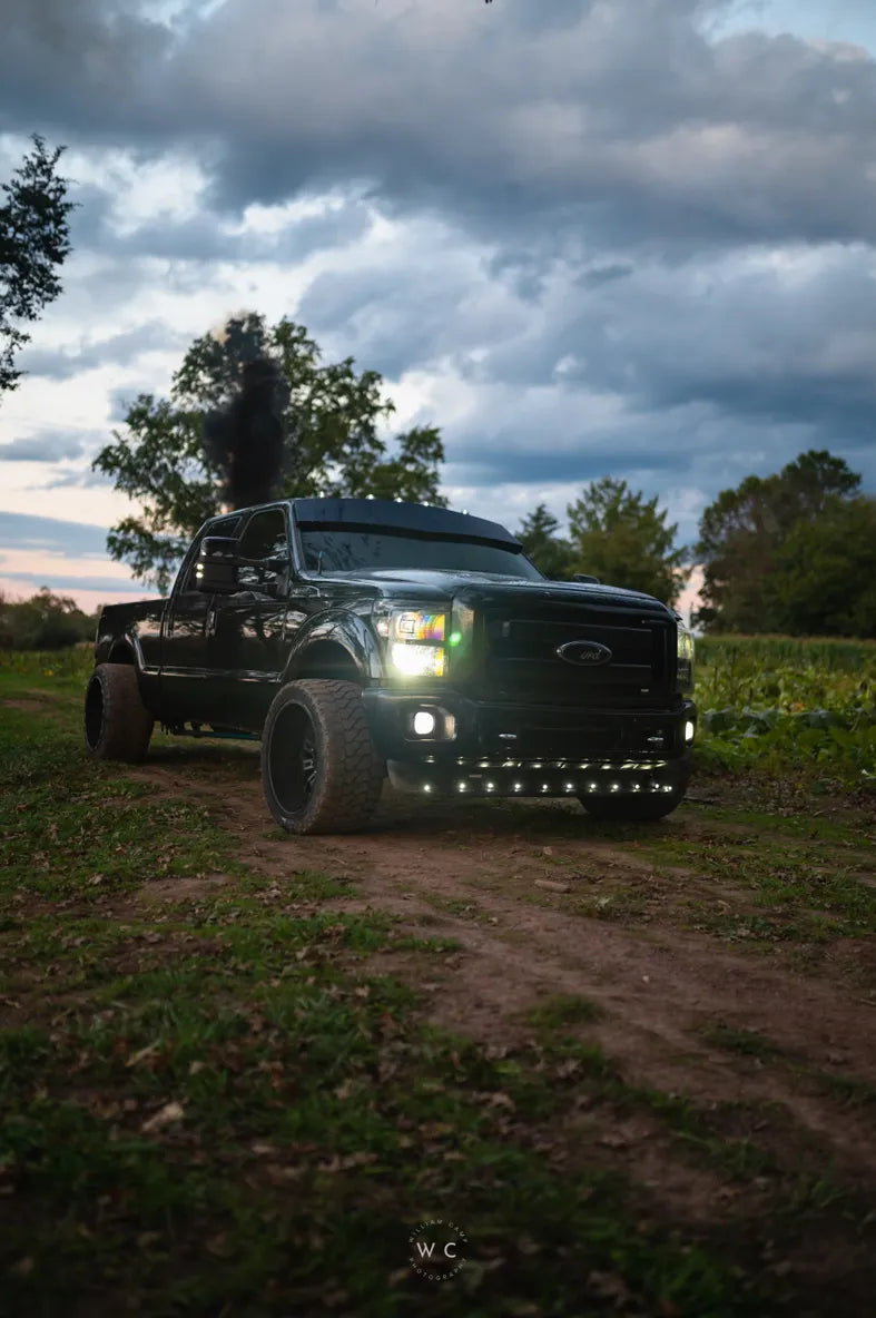 Lifted black pickup truck with LED lights and smoke exhaust on a dirt road at dusk