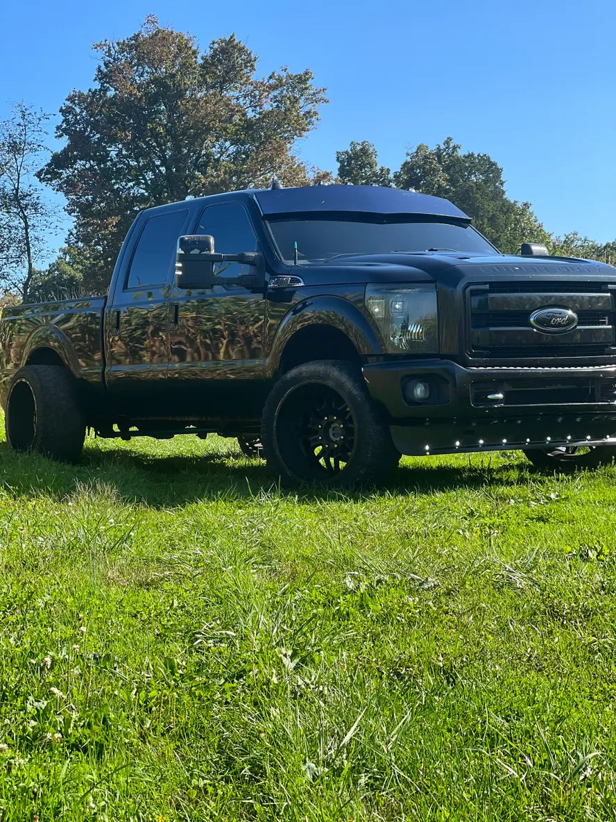 Black lifted pickup truck with tinted windows parked on grass under a clear blue sky