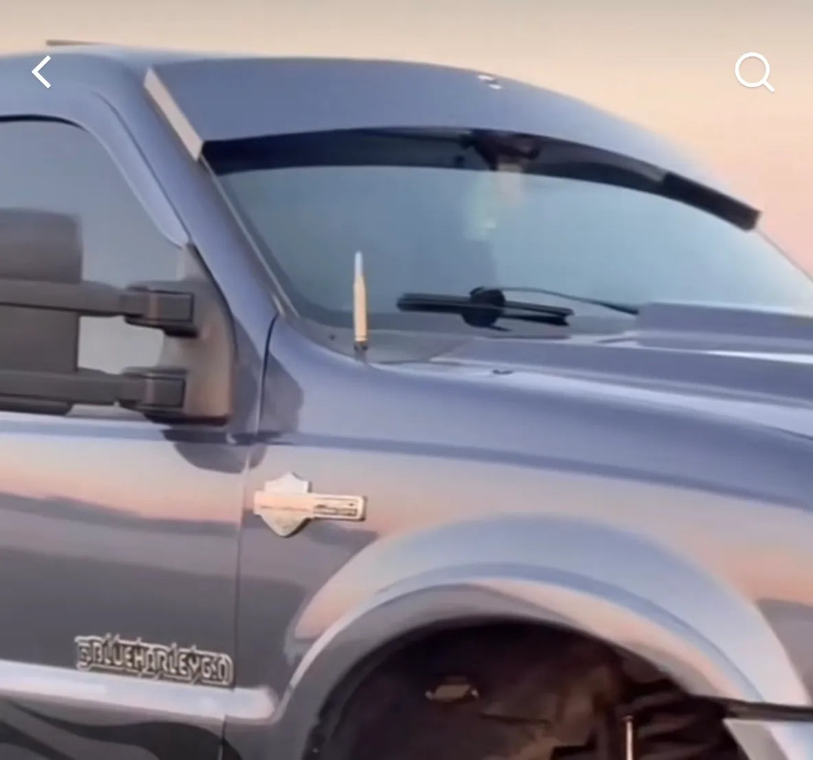 Close-up of dark gray pickup truck with custom side mirror and windshield visor at sunset