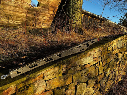 Steel off-road traction board on stone wall with dry grass and wooden structure in background