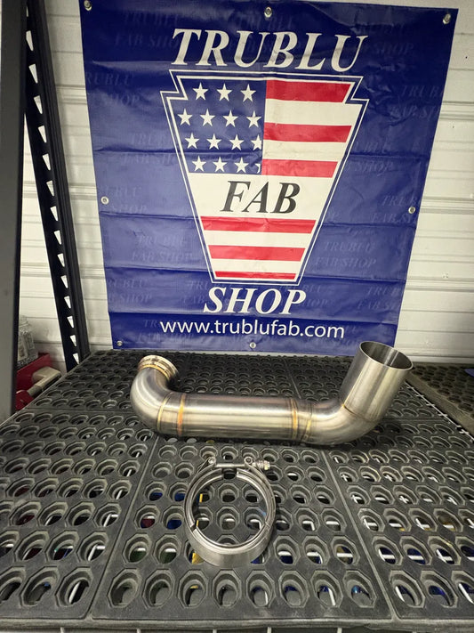 Stainless steel exhaust pipe with V-band clamp on a metal workbench in a fabrication shop.