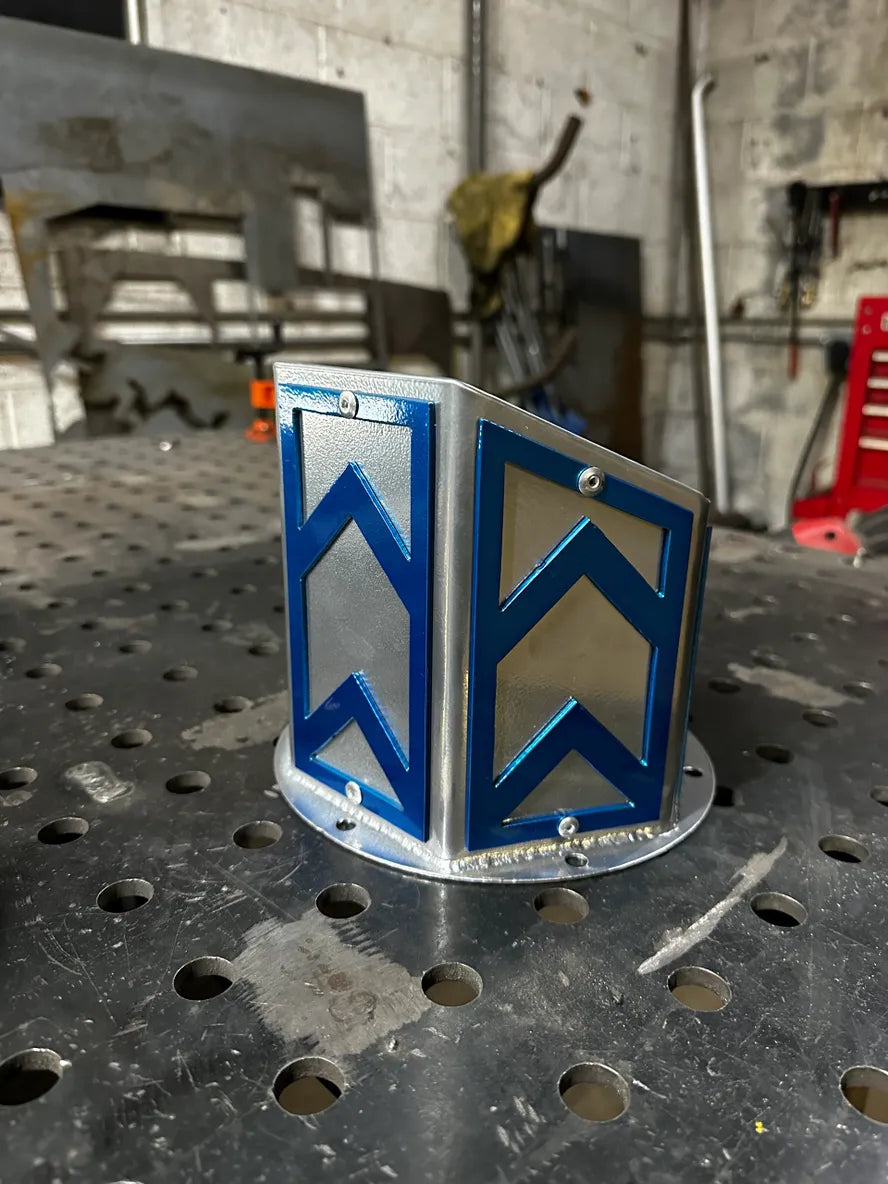 Custom metal fabrication part with blue arrow design on silver, displayed on workshop table