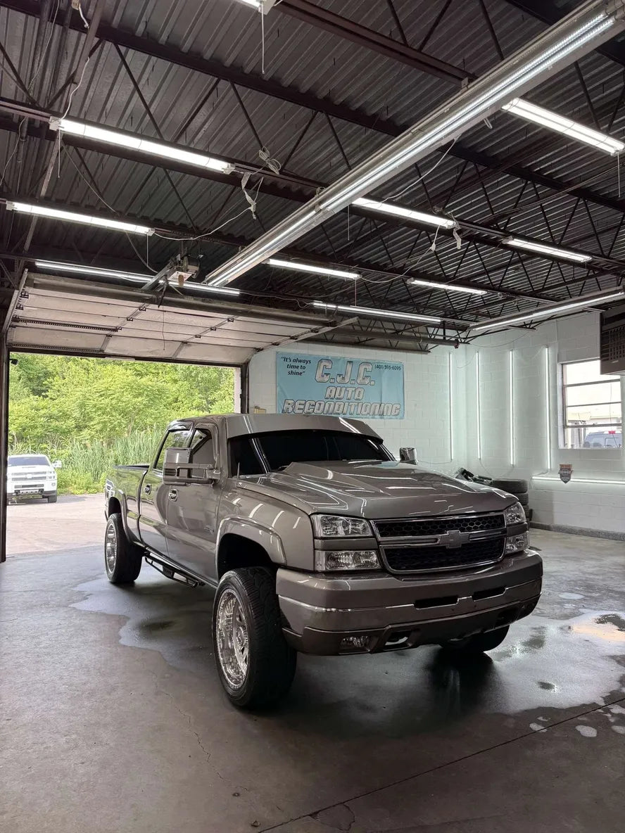 Silver lifted Chevrolet Silverado pickup truck with custom wheels parked in auto shop garage