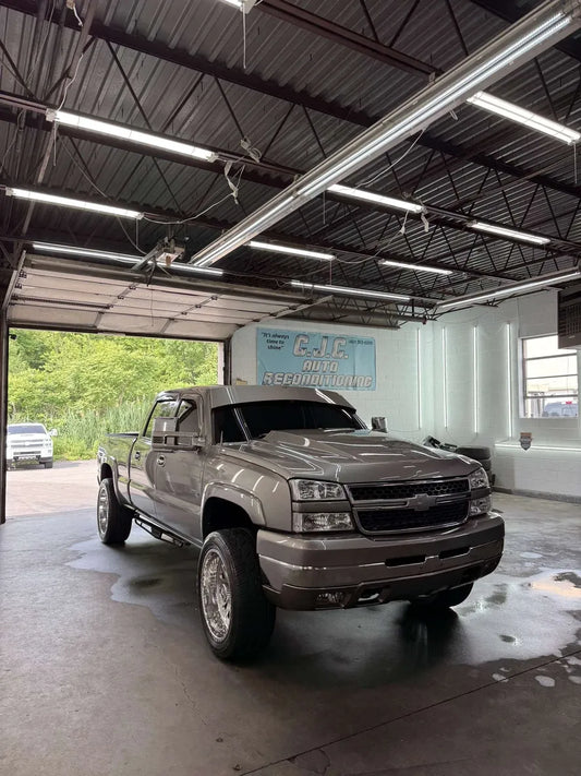 Silver lifted Chevrolet Silverado pickup truck with custom wheels parked in auto shop garage
