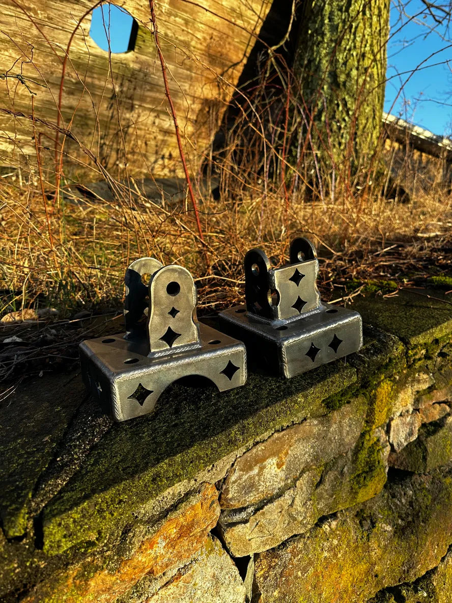 Two custom metal brackets with star-shaped cutouts on a mossy stone wall outdoors.