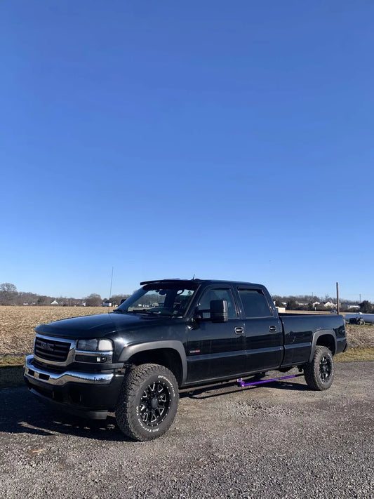 Black GMC pickup truck with off-road tires parked outdoors on gravel under a clear blue sky