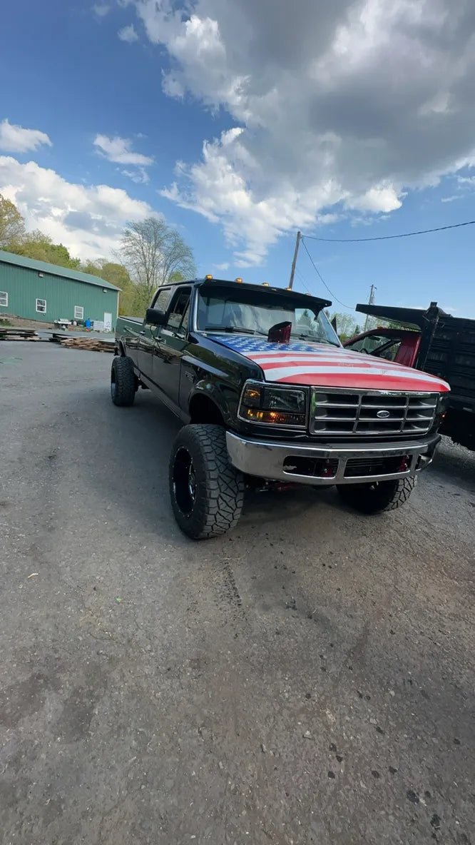 Lifted black Ford pickup truck with American flag hood parked outdoors on asphalt