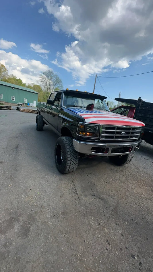 Lifted black Ford pickup truck with American flag hood parked outdoors on asphalt