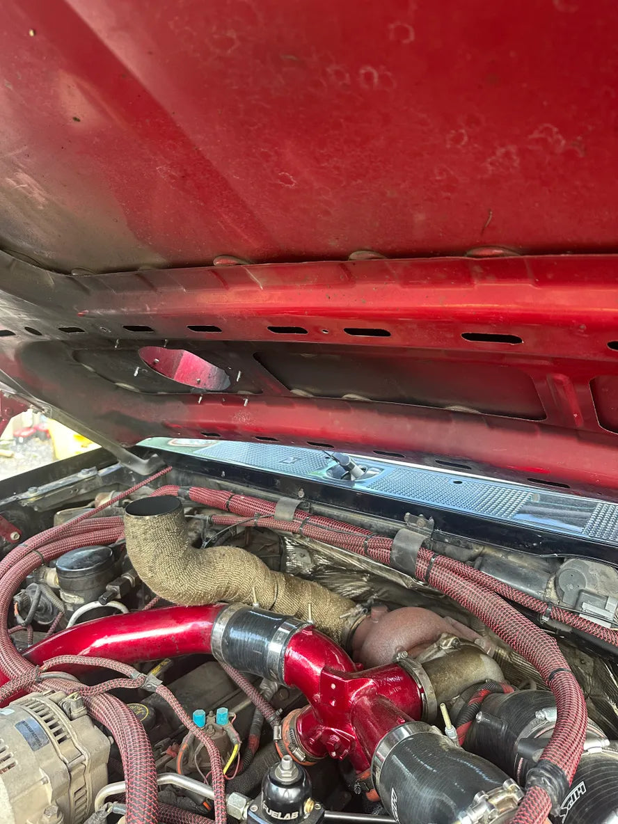 Close-up of a modified truck engine bay with red intake piping and heat-wrapped components