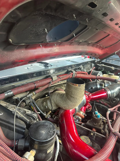 Aftermarket intake hood vent installed in the engine bay of a pickup truck with red piping.