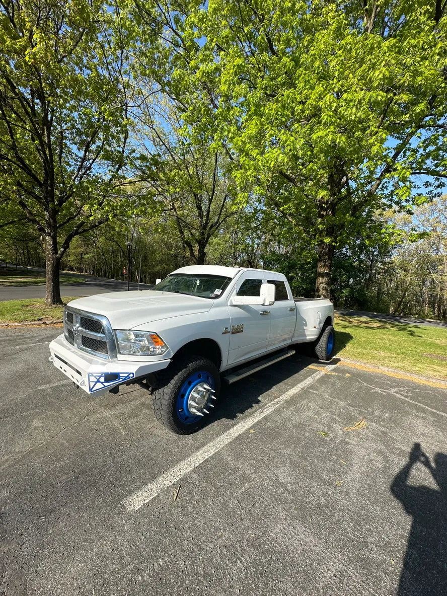 White pickup truck with custom blue wheel covers parked on asphalt under green trees