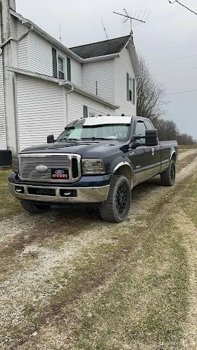 Black Ford pickup truck with chrome grille parked on gravel driveway beside a white house