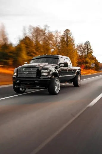 Black lifted pickup truck driving on highway with blurred autumn trees in background
