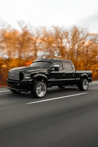 Black custom pickup truck with chrome wheels driving on highway, autumn trees in background