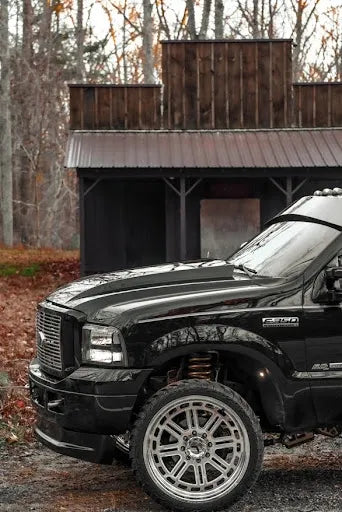 Black Ford F-250 pickup truck with custom wheels parked in front of rustic wooden building
