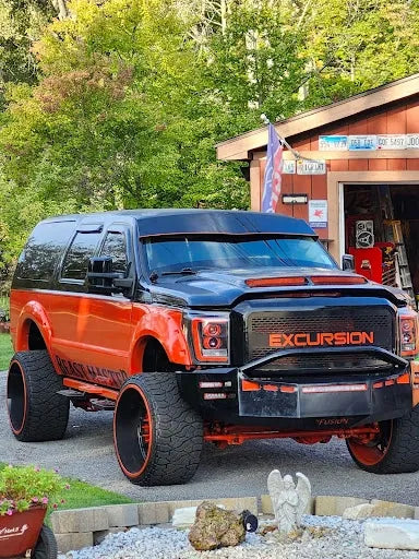 Custom orange and black lifted Ford Excursion SUV parked outdoors near a shop.