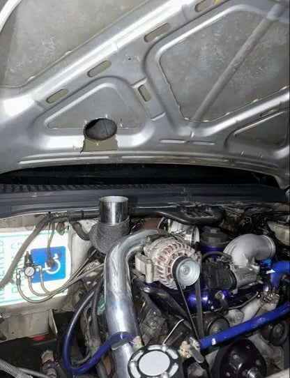 Modified car engine bay with custom turbo piping and hole cut in hood for clearance