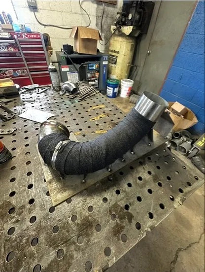 Custom fabricated exhaust pipe with heat wrap on a metal workbench in a workshop.