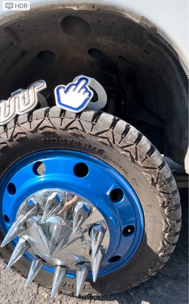 Blue truck wheel with chrome spiked hubcap and novelty middle finger sign on tire