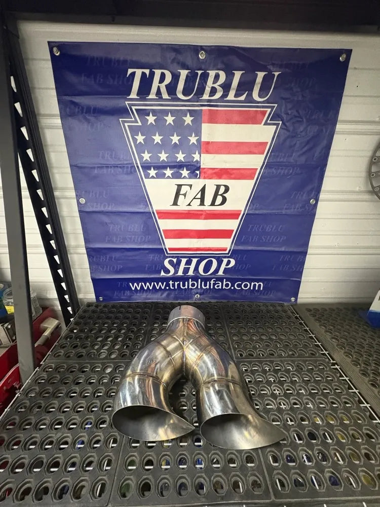 Stainless steel Y-pipe exhaust component on metal workbench in fabrication shop setting