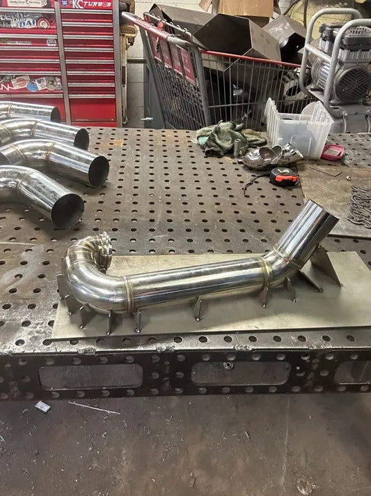 Stainless steel custom exhaust pipe on a fabrication workbench in an automotive workshop