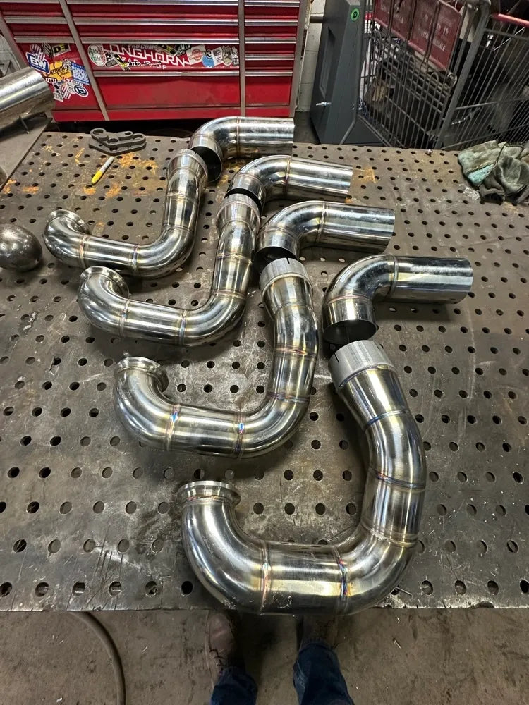 Welded stainless steel exhaust pipes with bends on a perforated metal workbench in a workshop