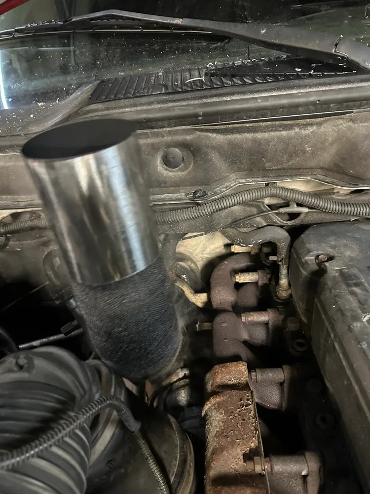 Closeup of custom exhaust stack and rusted exhaust manifold in a truck engine bay