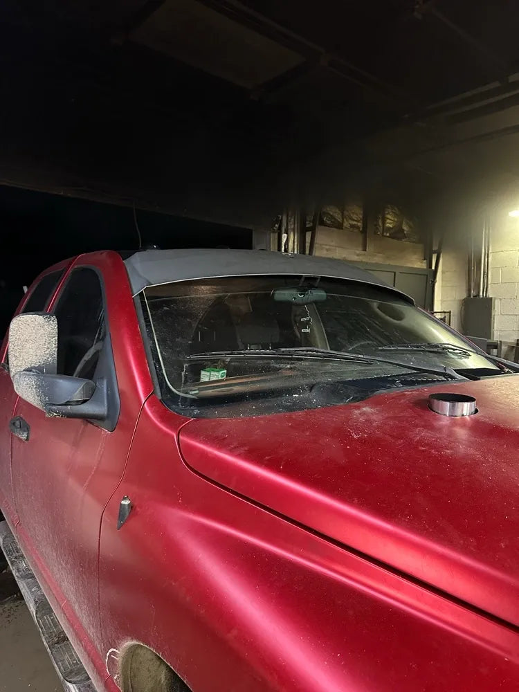 Red pickup truck with dusty exterior parked indoors, featuring a custom windshield and hood detail.