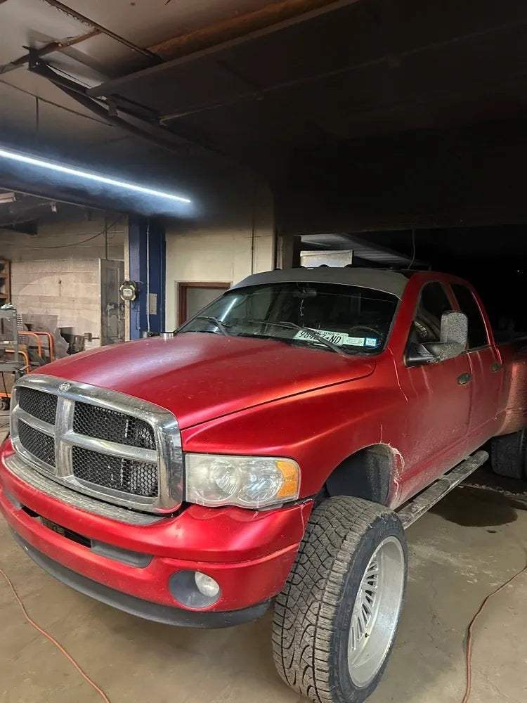 Red pickup truck with large custom wheels in an indoor automotive workshop setting.