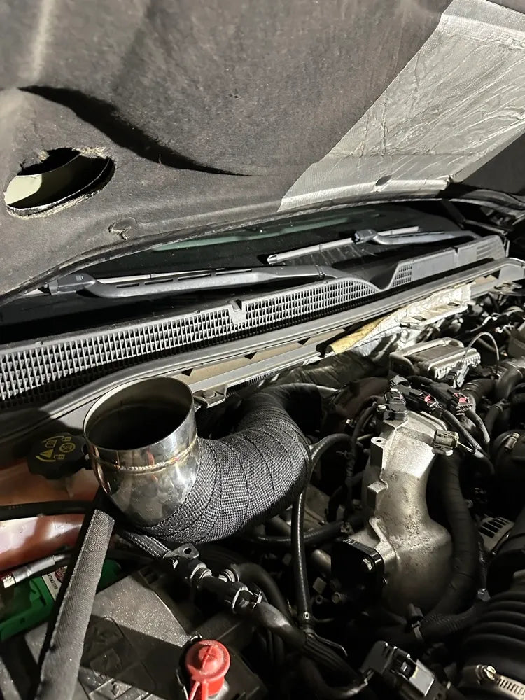 Close-up of a car engine bay with custom wrapped turbo piping and exposed intake components.