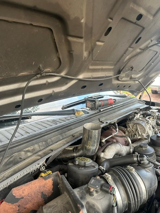 Close-up of a truck engine bay with aftermarket turbo piping and power tools on the cowl