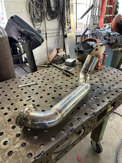 Polished metal exhaust pipe on perforated metal workbench in fabrication workshop