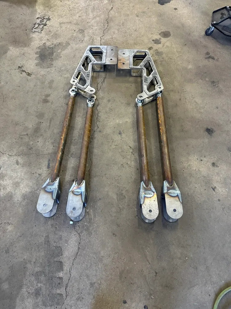 Heavy-duty metal suspension link brackets with four attached steel control arms on workshop floor