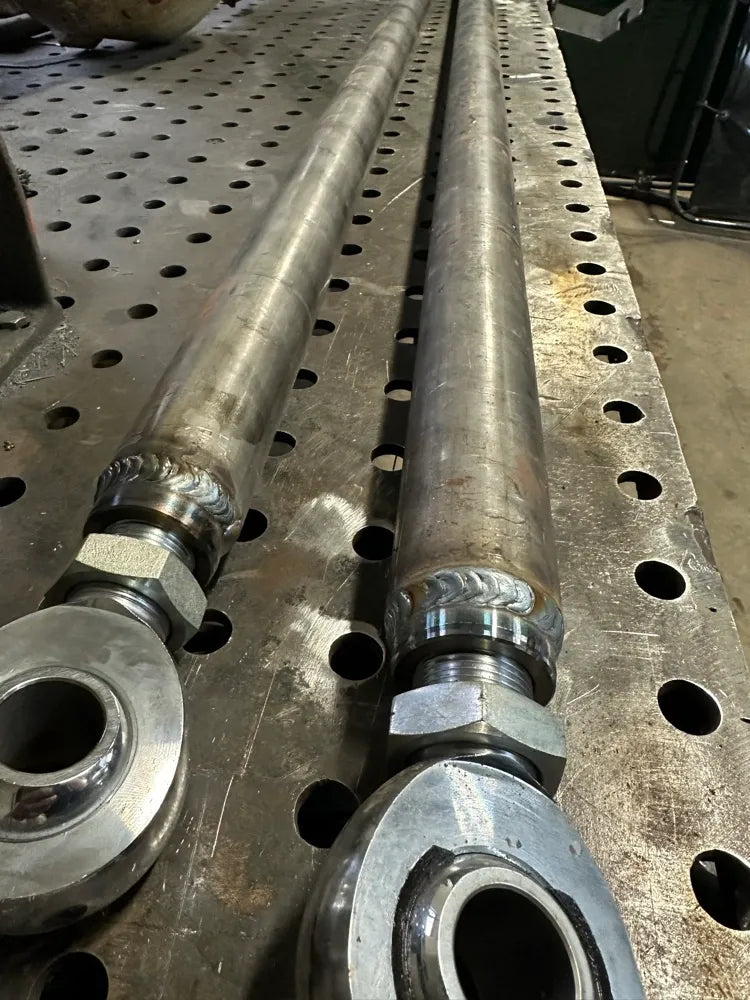 Heavy-duty metal tie rods with heim joints on perforated welding table, fabrication shop setting