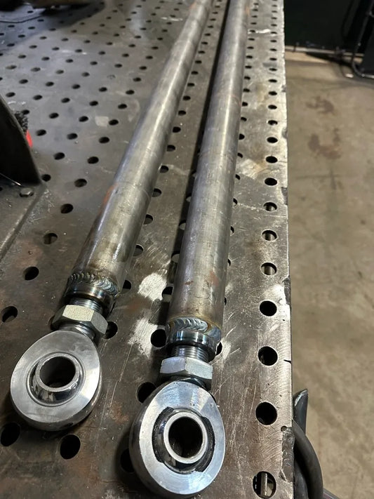 Pair of heavy-duty steel rod ends with heim joints on a perforated metal workbench