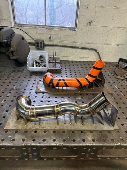 Metal exhaust pipe fabrication and orange mockup on a welding table in workshop