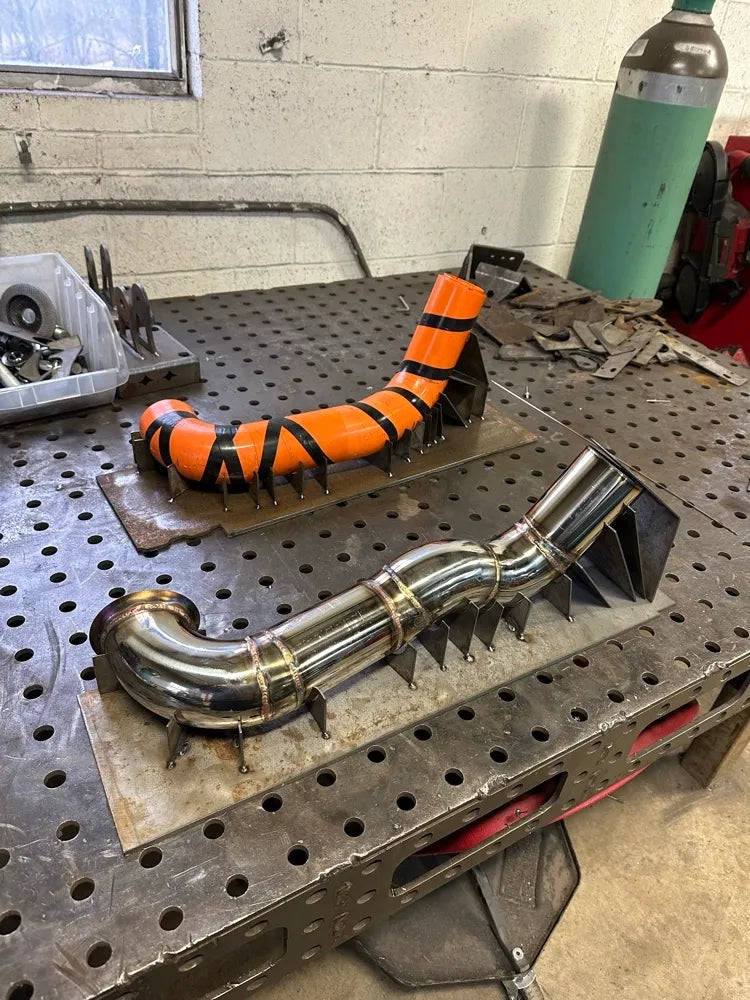 Welded metal exhaust pipe and orange mockup on fabrication table in metal workshop