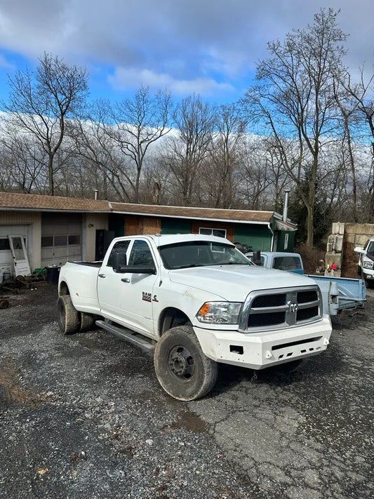 White heavy-duty pickup truck with aftermarket bumper parked on gravel near workshop and trees